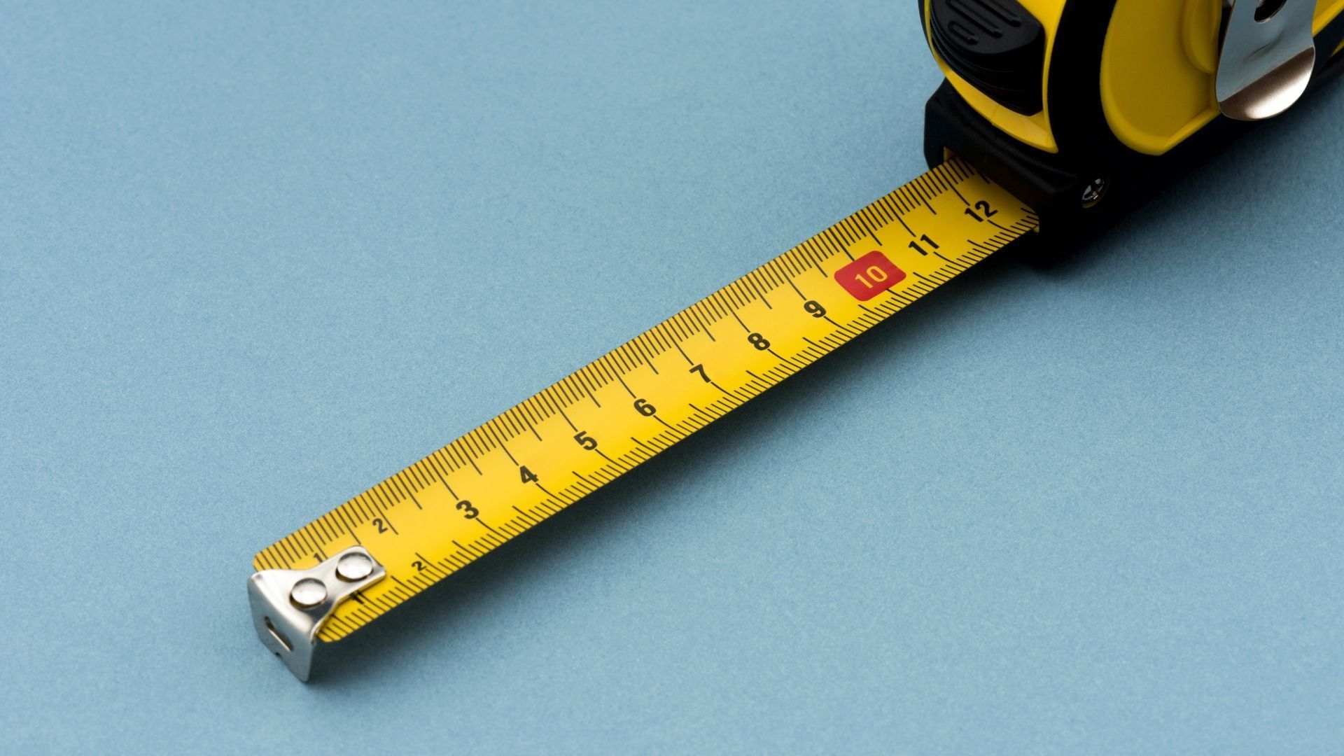 Yellow and black tape measure extended, showing a measurement of 10 inches against a blue background.