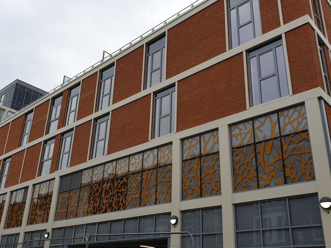 Red brick building with rows of windows and decorative paneling on a cloudy day.