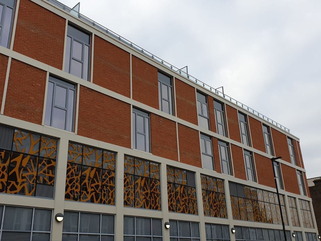 Brick building with rectangular windows and decorative panels on the bottom floor under a cloudy sky.