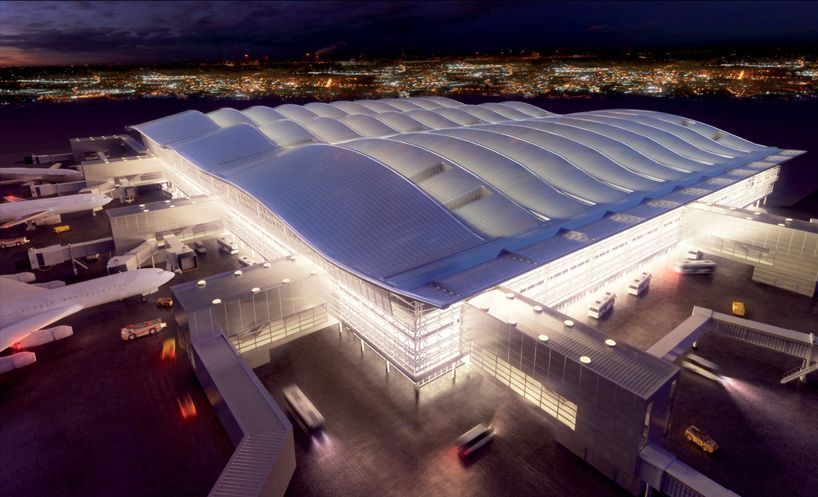 Airport terminal lit up at night, with a curved roof and city lights in the background.