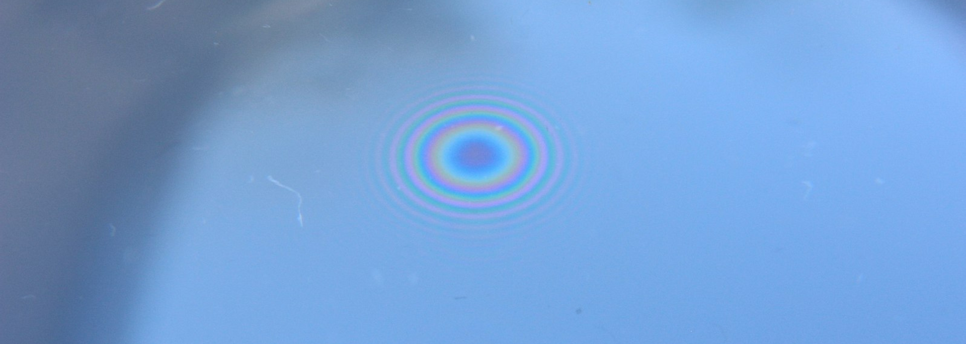 A blue surface with a circular pattern of colored rings, reflecting light.