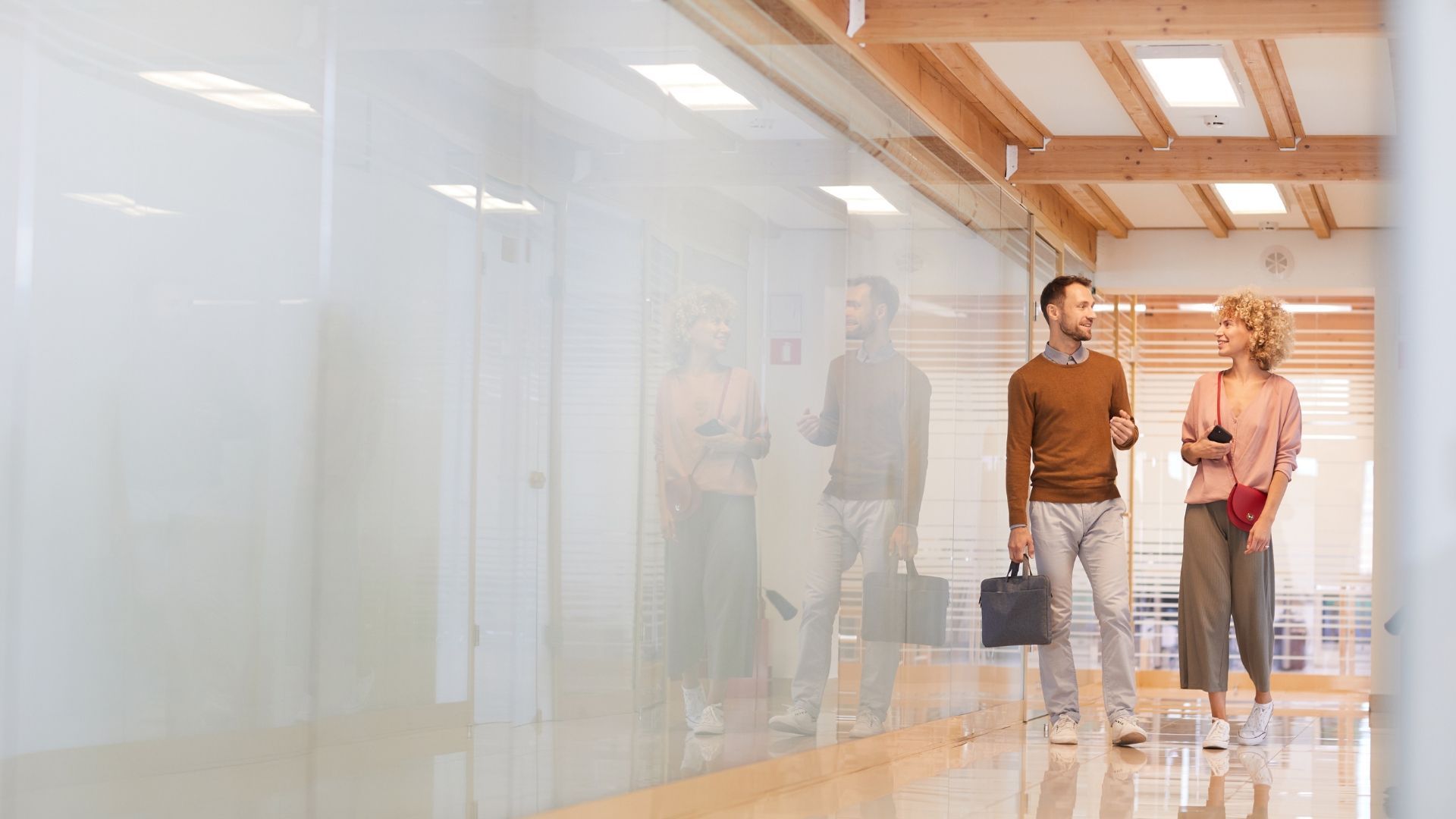Two people walking in a hallway, one carrying a briefcase, the other holding a small notebook.