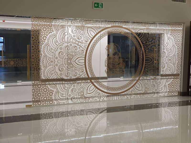 Glass wall with ornate gold decorative pattern, reflecting the interior and floor.