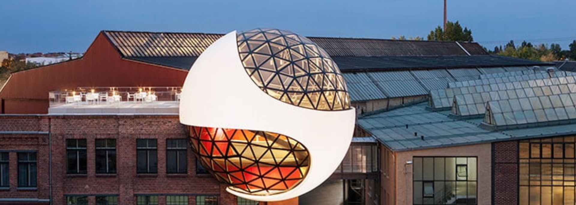 A large, geometric, spherical structure is attached to a brick building. It has a white exterior with a clear, patterned glass section.