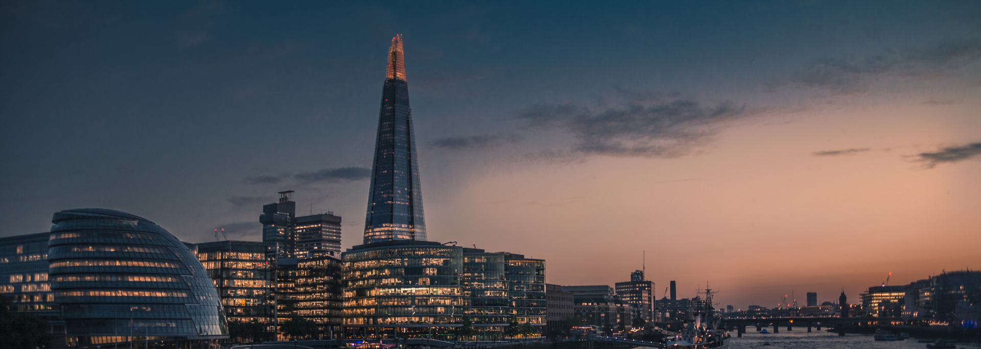 London skyline at dusk, with the Shard illuminated. The sky is a mix of blue and orange.
