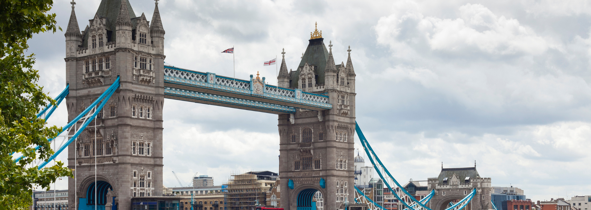 Tower Bridge in London, England. Gray stone bridge with blue suspension cables against a cloudy sky.