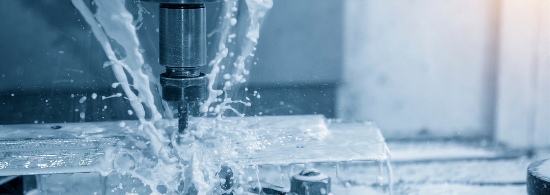 A CNC machine drilling into metal with coolant spraying.