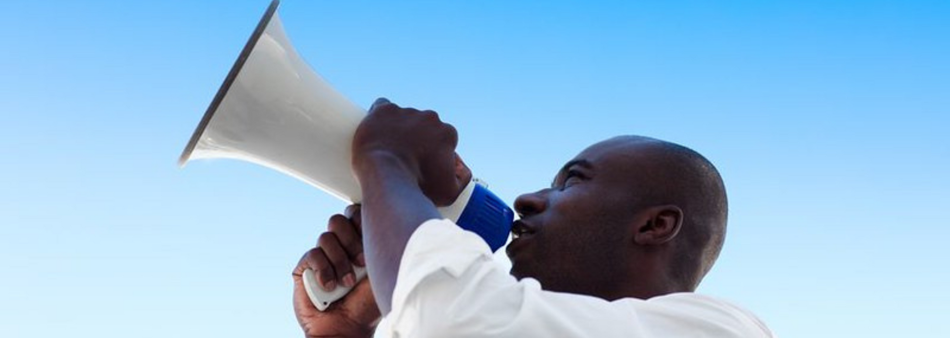 Man holding a megaphone, speaking against a blue sky.