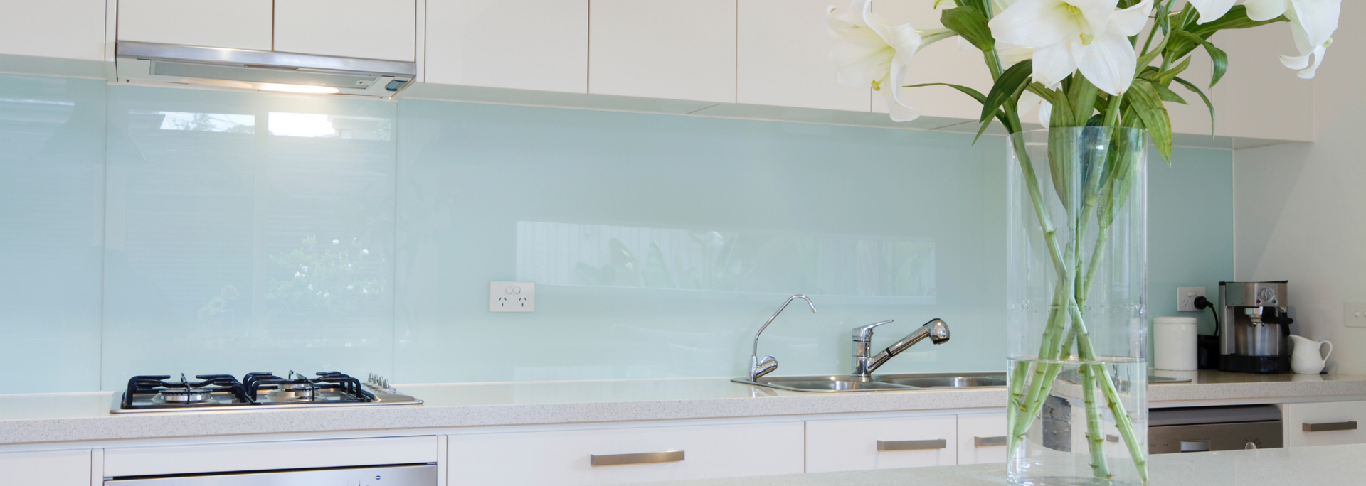 Kitchen interior with white cabinets, light blue backsplash, and a vase of white lilies.