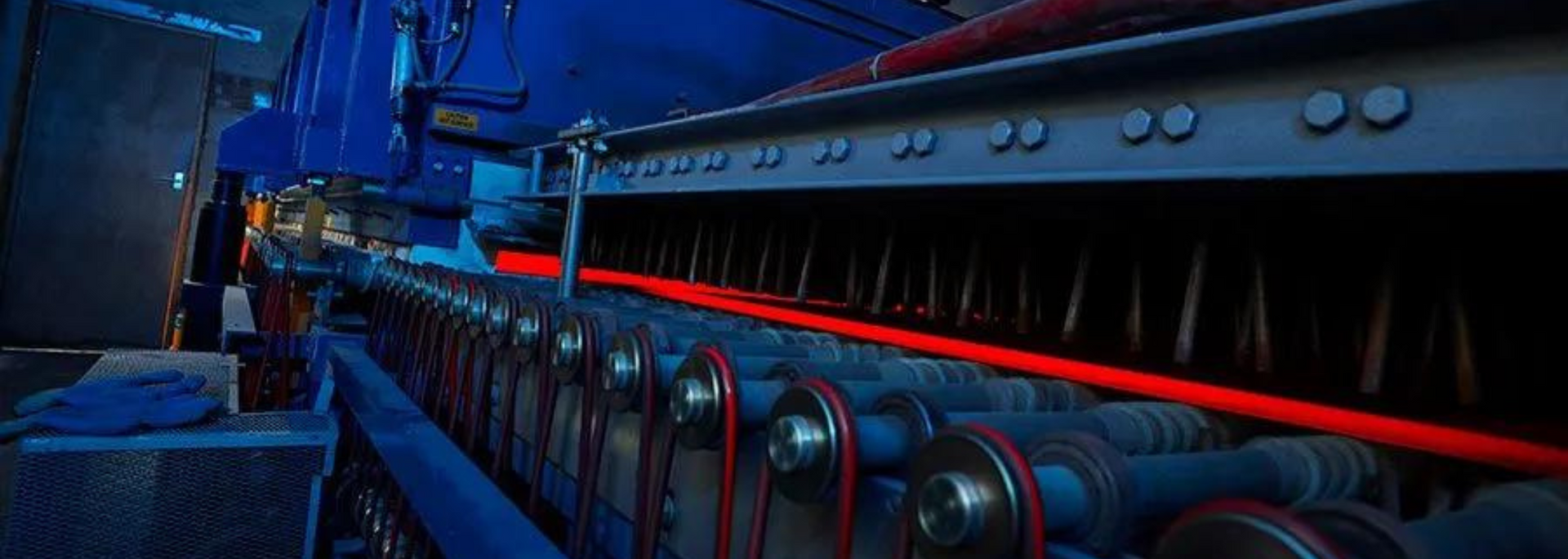 Glowing red-hot metal bar being processed in a factory setting.