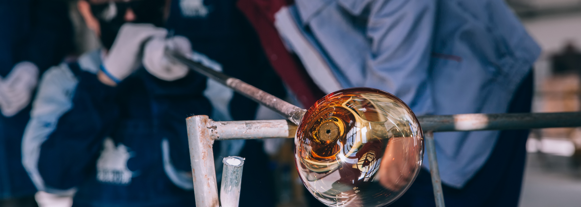 Glassblowing, molten glass being shaped by a craftsperson using a long metal rod.