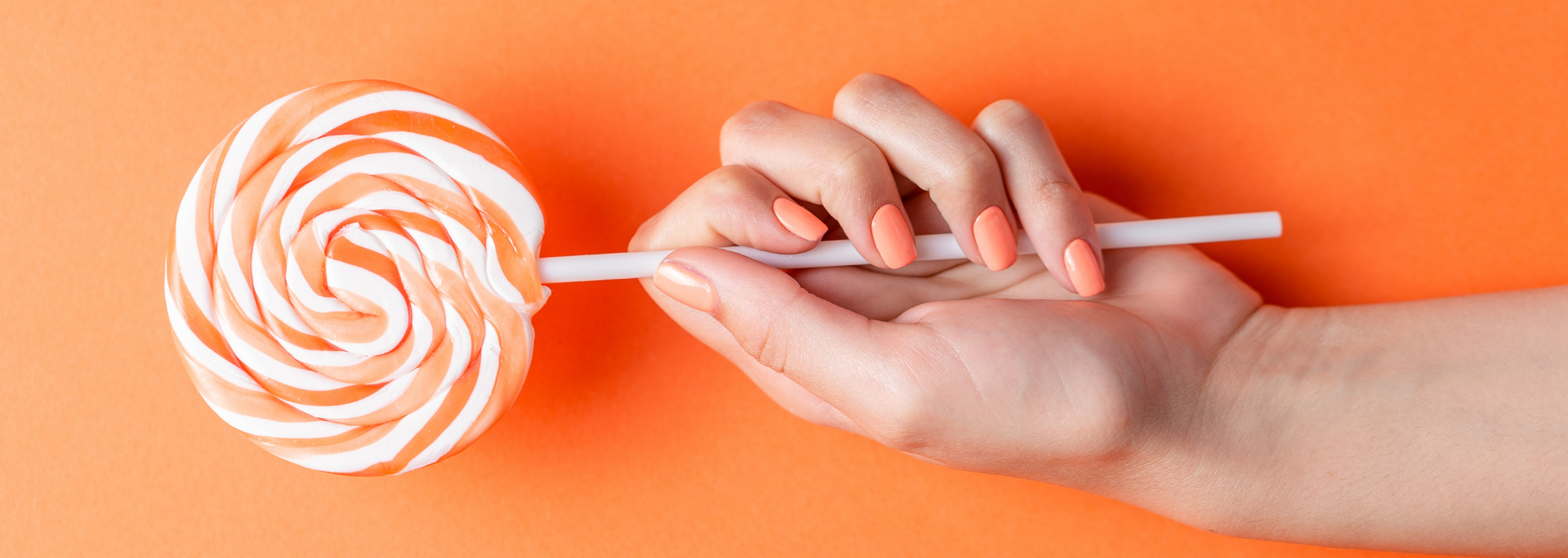Hand holding a lollipop with peach and white swirl on an orange background.