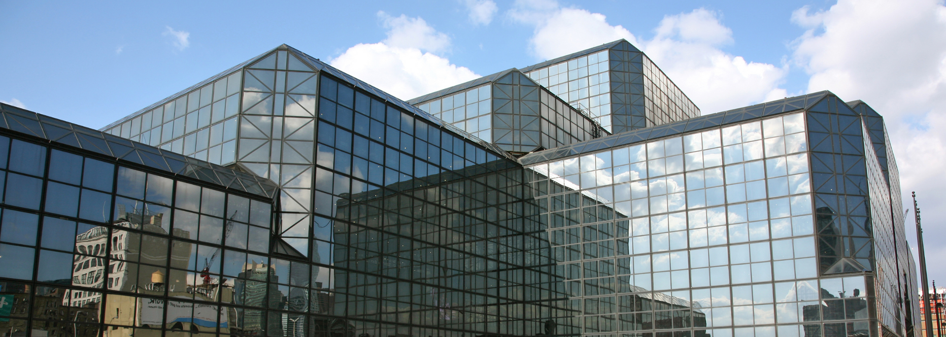 Modern building with glass walls reflecting the sky and other structures.