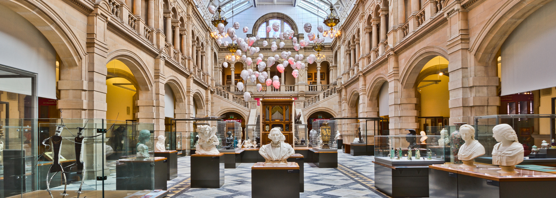 Museum interior with busts on display, arched architecture, glass ceiling, and decorative balloons.