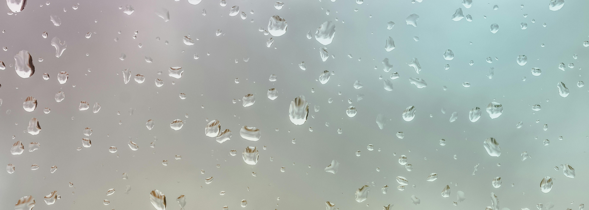 Close-up of glass surface with many clear water droplets, on a faded background with pale colors.