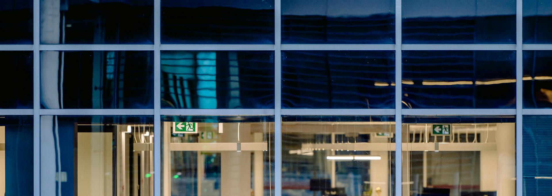 Exterior view of a building with a grid of windows. Inside are signs and lights.