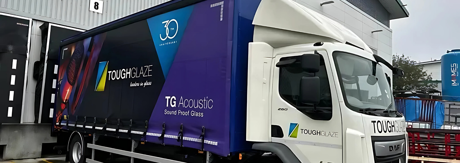 A white delivery truck with a trailer, branded with a company logo, backed into a loading dock.