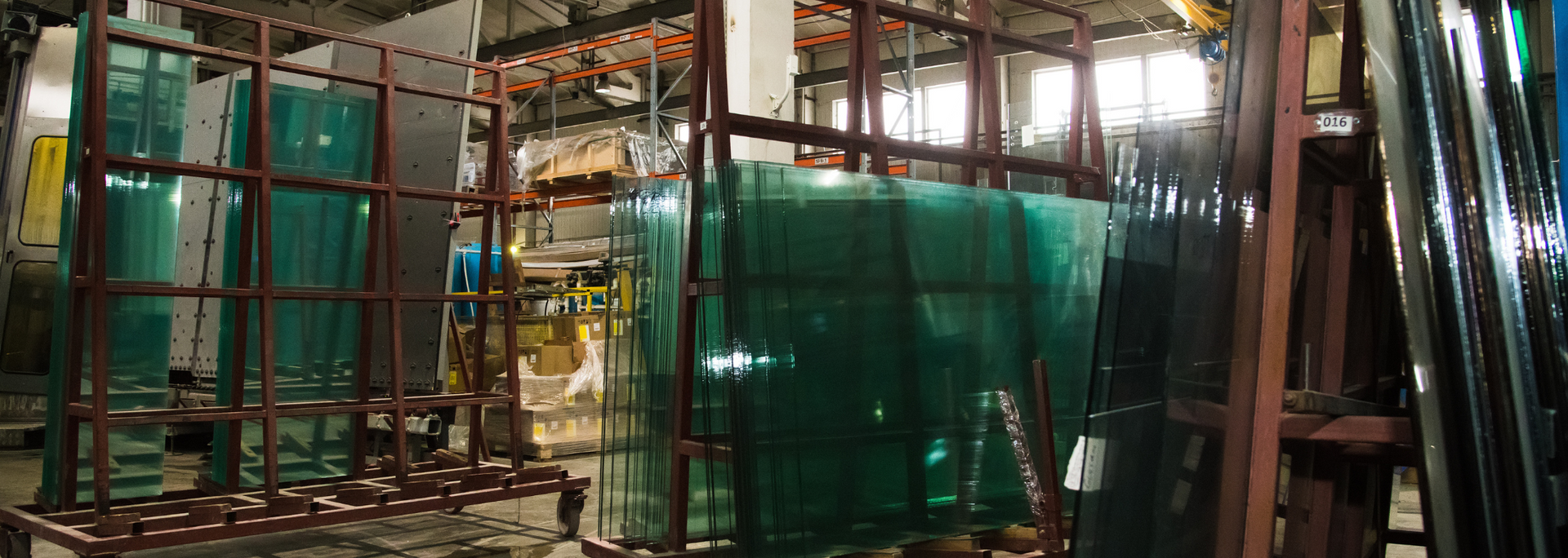 Stacks of green glass sheets in an industrial setting, held by metal frames.