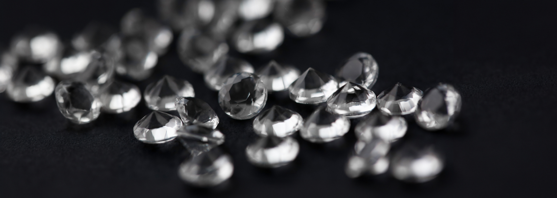 Close-up of sparkling clear gemstones scattered on a dark surface.