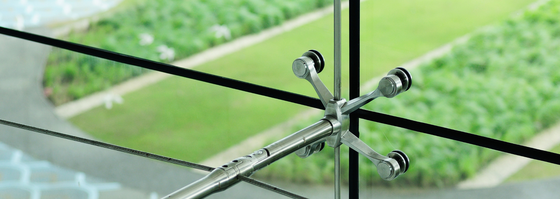 Metal spider fitting holding glass panels, showing a green lawn outside.