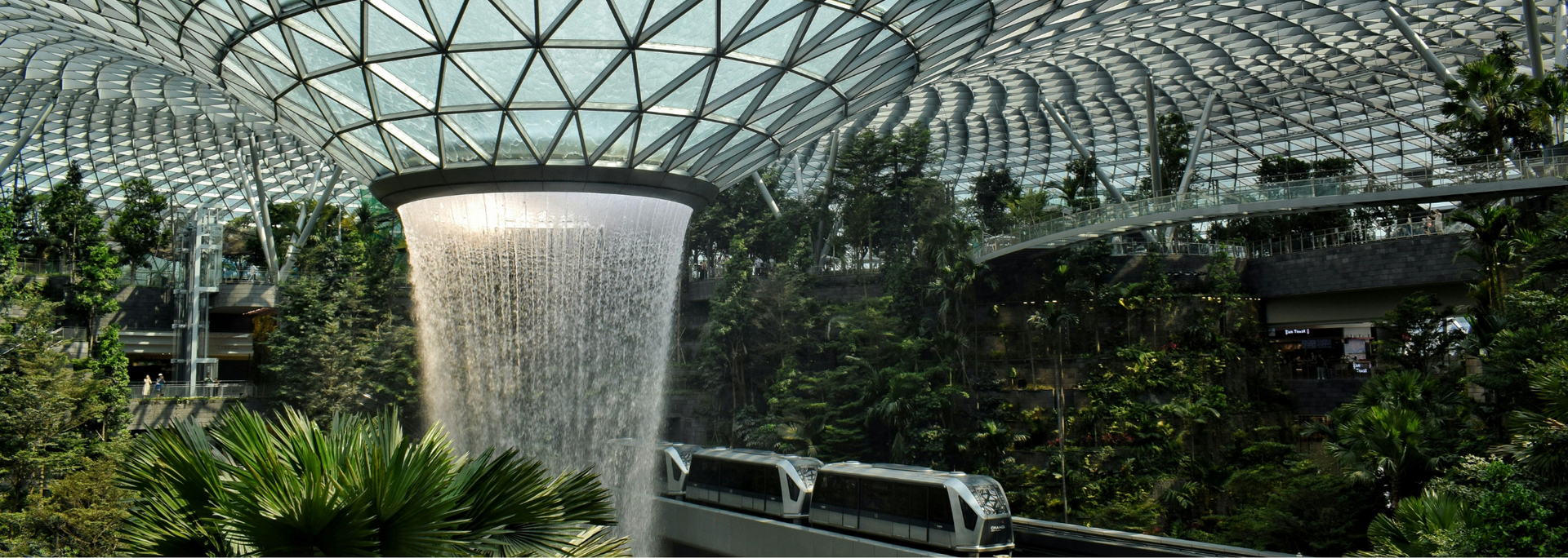 Waterfall cascading into a lush, indoor garden. A monorail car passes through the scene under a glass dome.