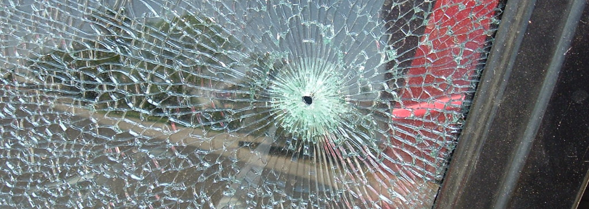 Shattered glass window with a central hole, red and black frame visible.
