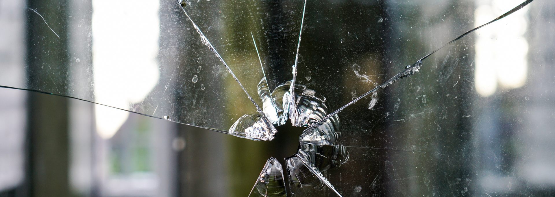 Close-up of a shattered window pane with a visible hole and radiating cracks.