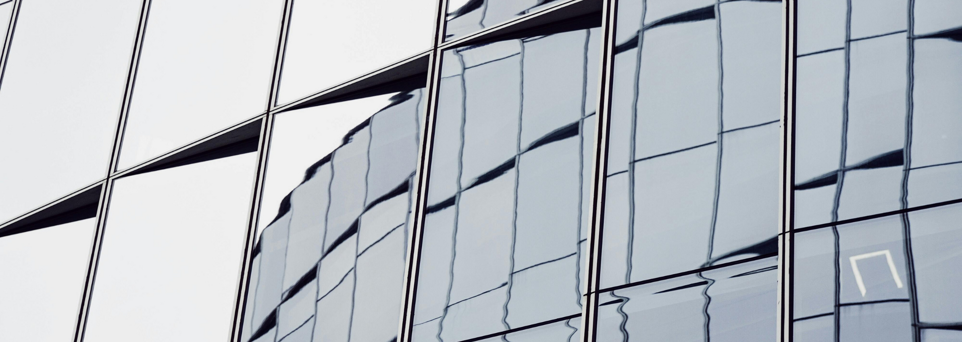 Close-up of a modern skyscraper's glass facade reflecting the sky; cool color palette with grid pattern.
