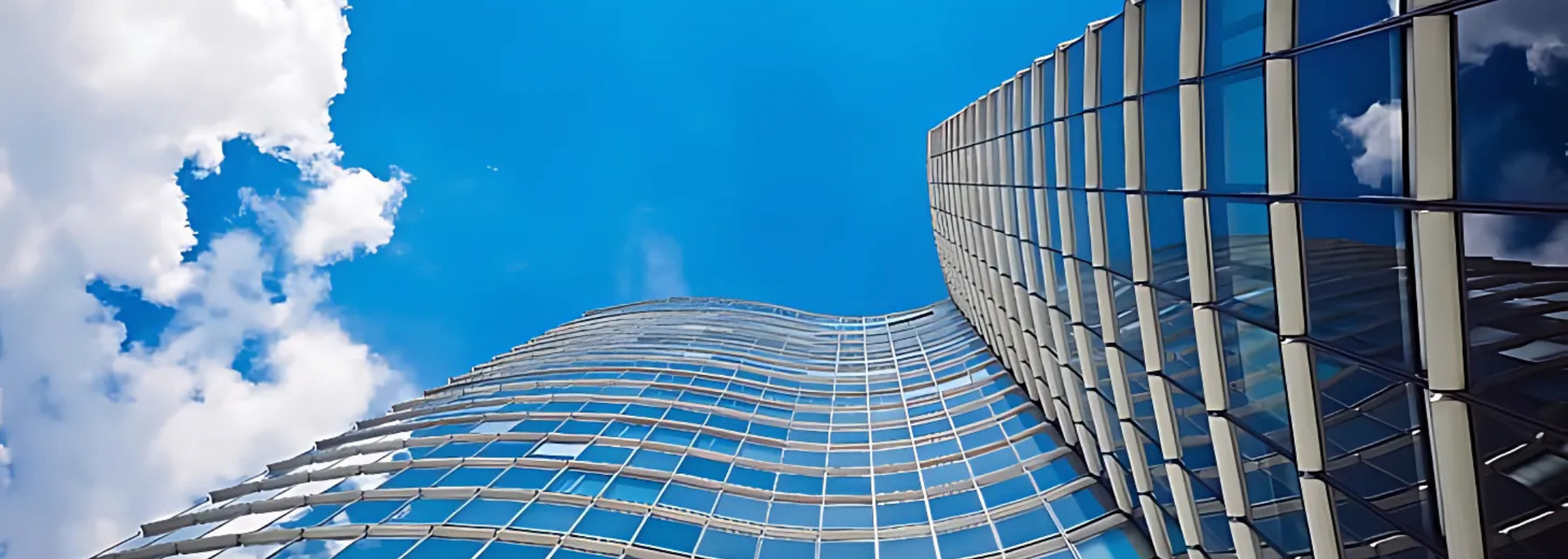 Modern glass skyscraper against a bright blue sky with scattered white clouds.
