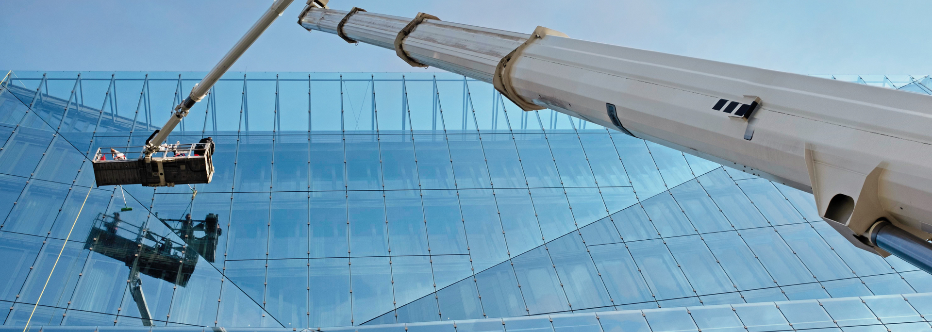 A window washing machine cleans a large glass-paneled building with a clear blue sky.