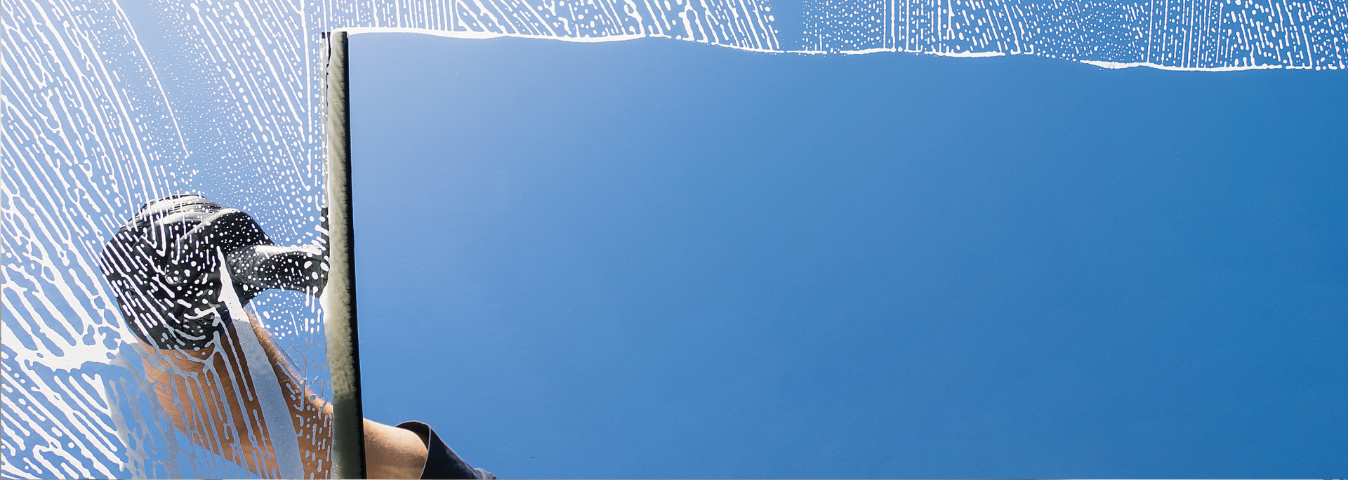 Window cleaner wiping a pane with a blue sky visible through the clear section.
