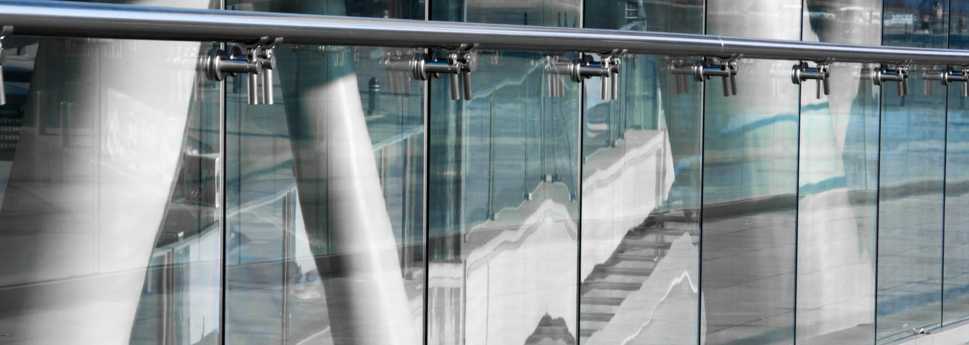 Glass railing with stainless steel handrail, reflecting a modern building.