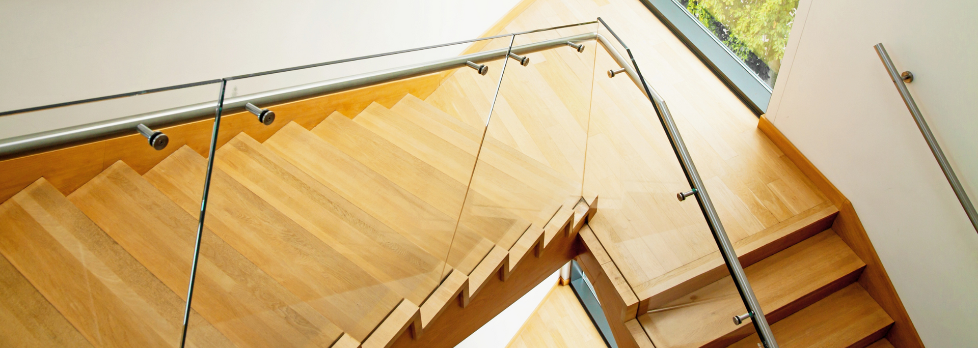 Wooden staircase with glass railing. Sunlight highlights the natural wood tones of the steps.