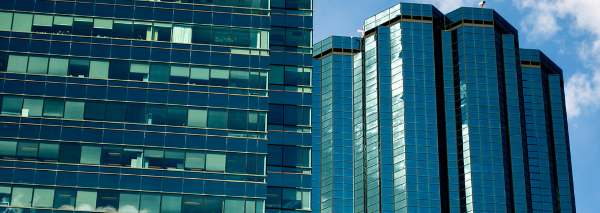 Two tall, blue glass skyscrapers against a blue sky with some clouds.