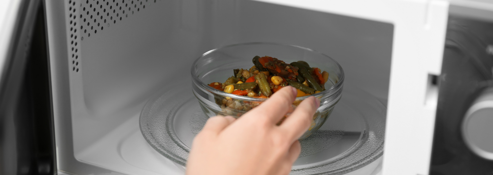 A person placing a glass bowl of food into a microwave oven.