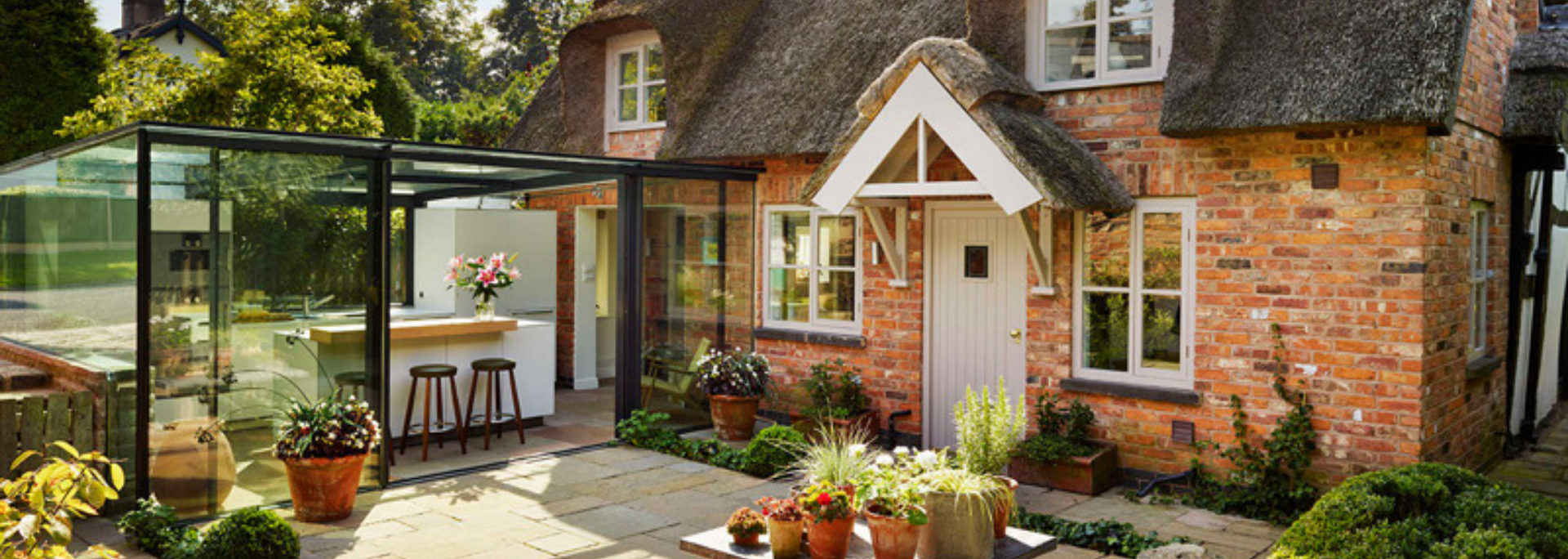 Quaint brick cottage with a thatched roof and an outdoor seating area.