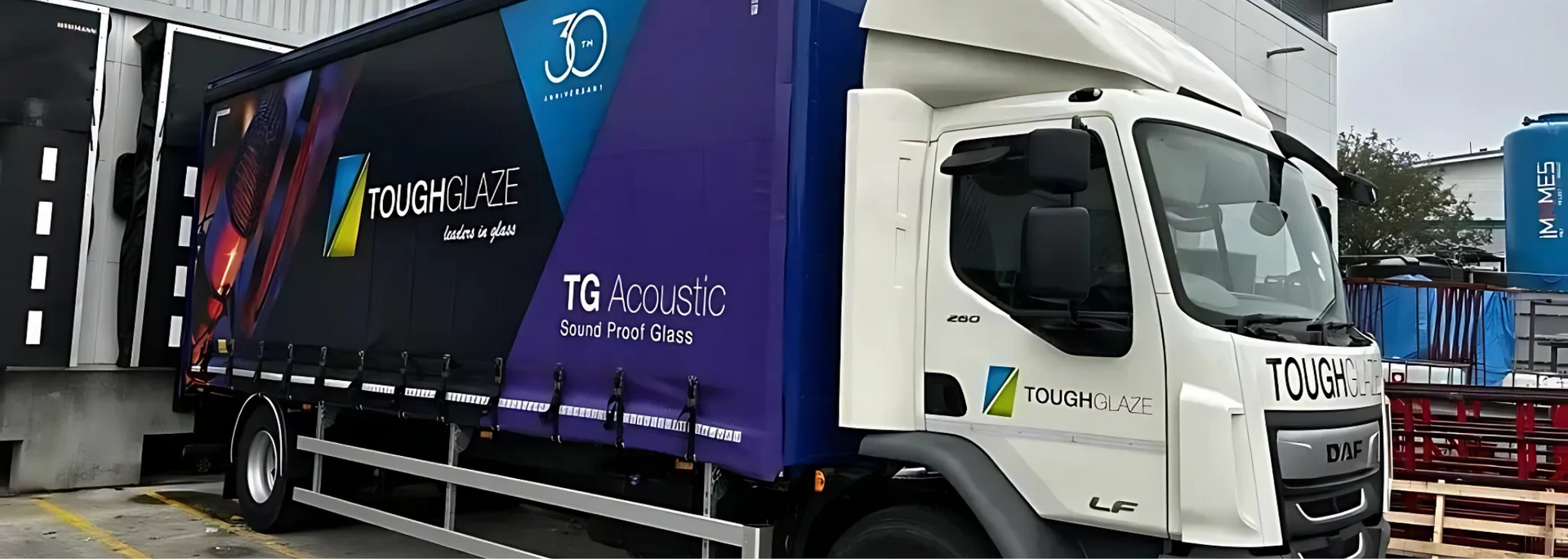 A white and purple T&G Acoustics delivery truck parked near a loading dock.