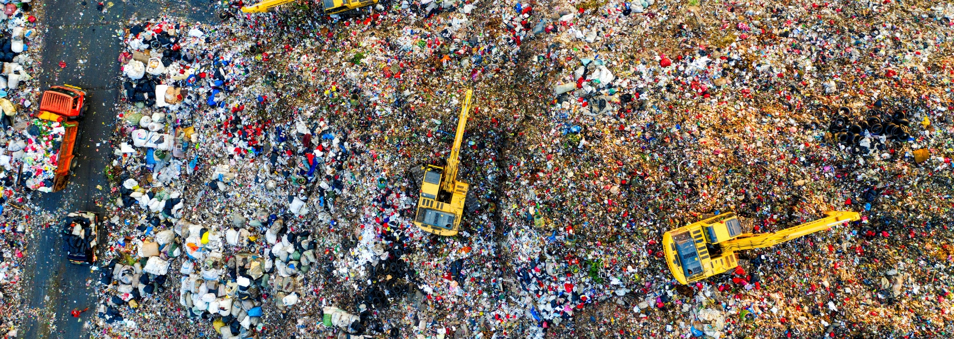 Aerial view of a landfill with multiple yellow excavators working among piles of garbage.