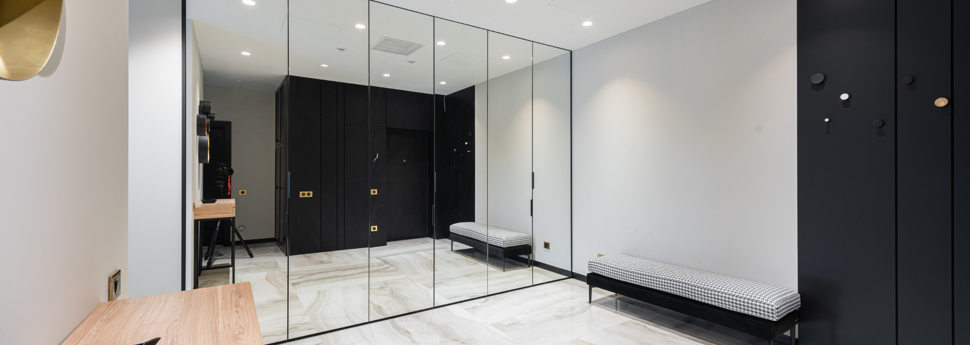 A modern hallway with mirrored walls, benches, and black storage cabinets.