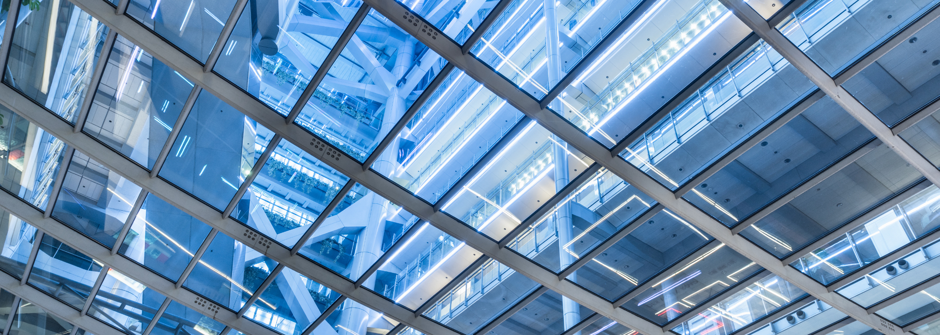 Looking up through a glass ceiling of a modern building, with blue hues and geometric patterns.