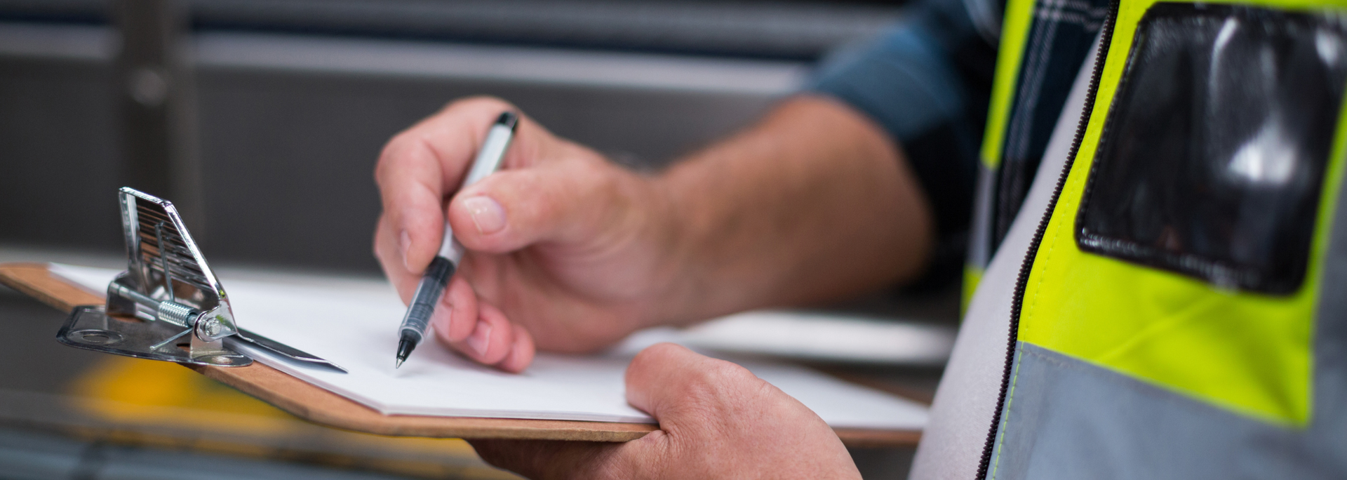 Person writing on a clipboard, wearing a safety vest.