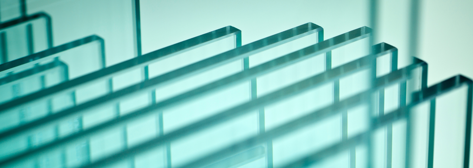 Stack of clear glass sheets, with blue-green hues and reflecting light.