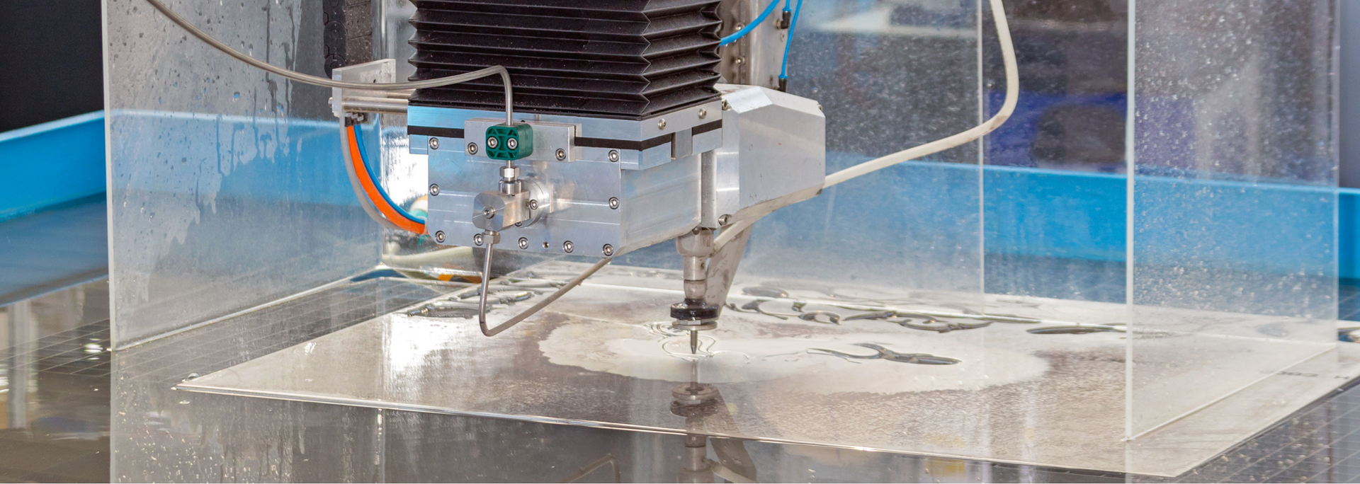 An industrial water jet cutter cutting a thick, light-colored material. Water spray surrounds the cutting area.