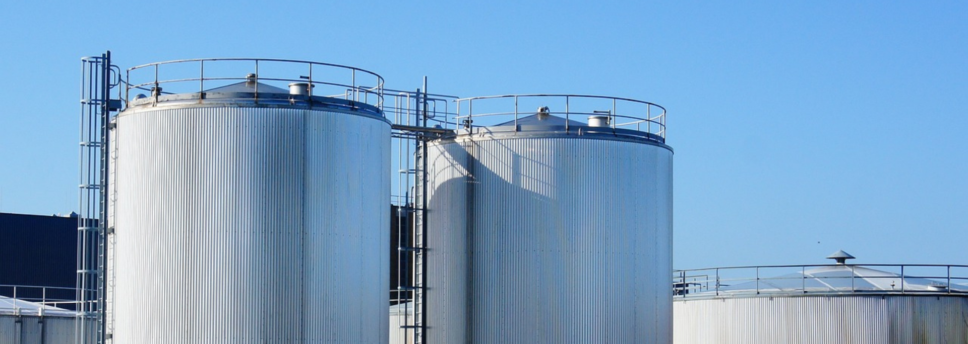 Three large, silver storage tanks with ladders, against a clear blue sky.