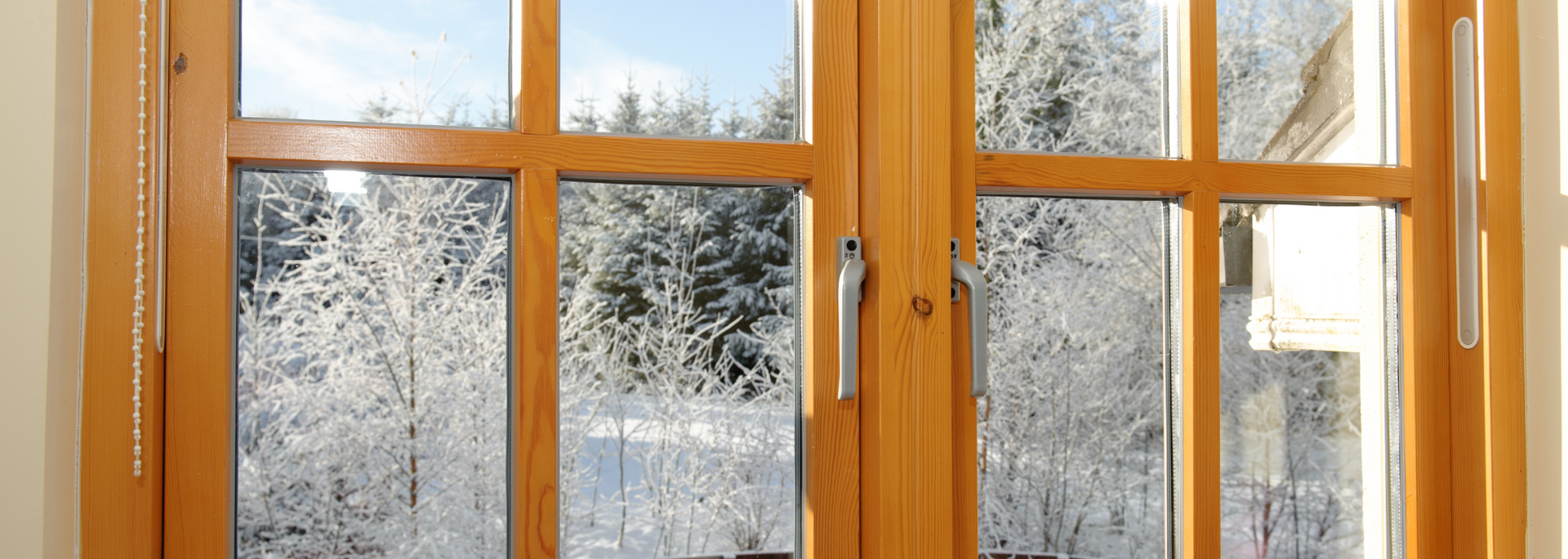 Wooden window frames with a view of snow-covered trees and a blue sky.