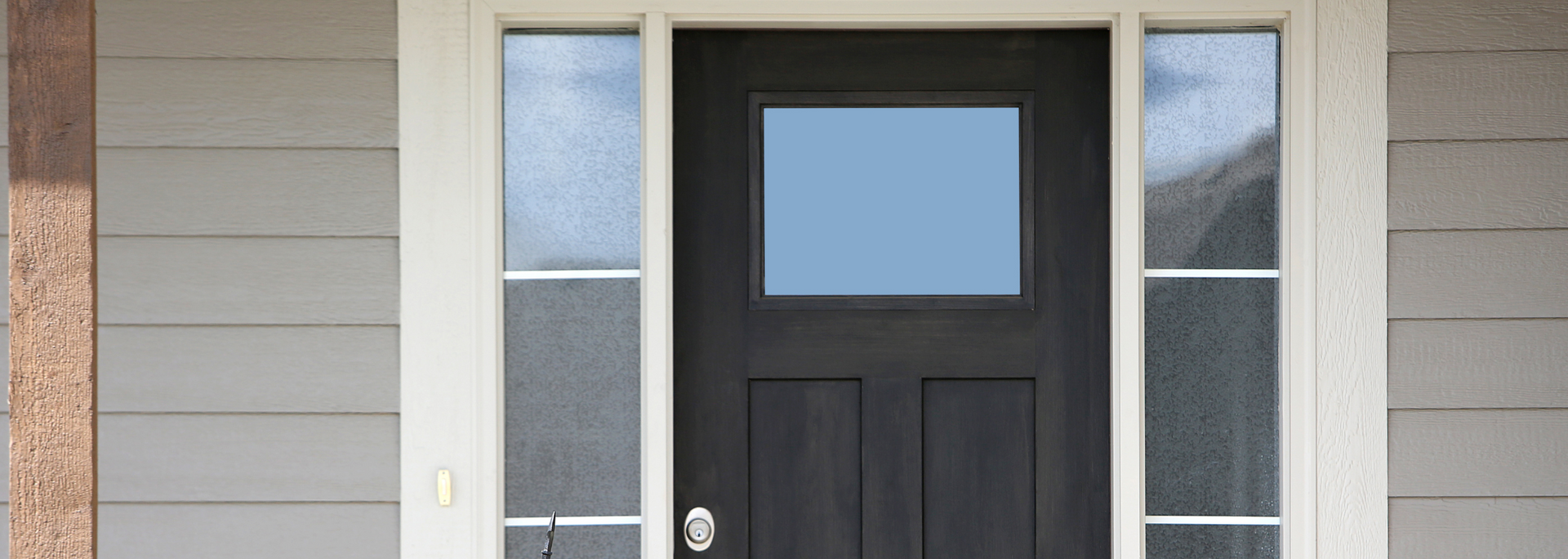 A black front door with a square window, flanked by two narrow windows, on a gray house.