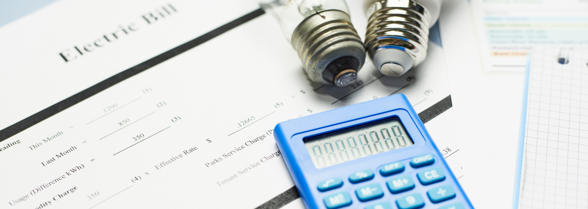 Blue calculator on an electric bill with light bulbs, suggesting cost analysis.