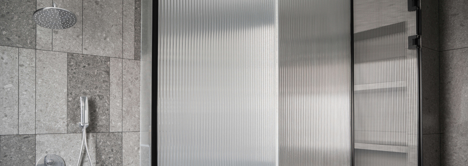 Shower with textured stone wall, circular rain shower head, and vertical ridged glass panel.