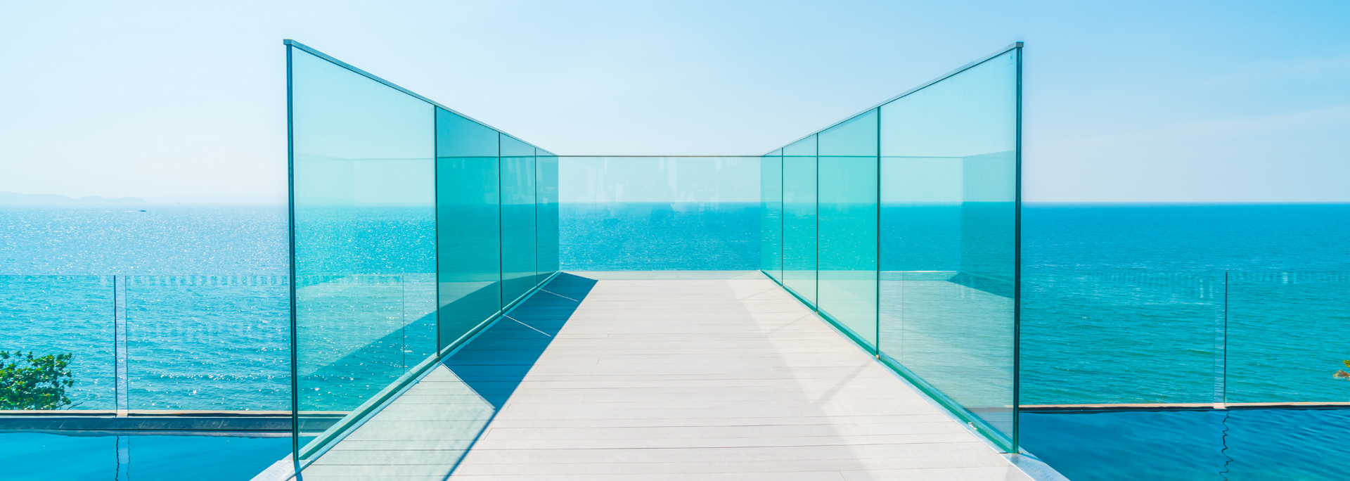 A walkway with glass walls and the ocean in the background. The sky is blue.
