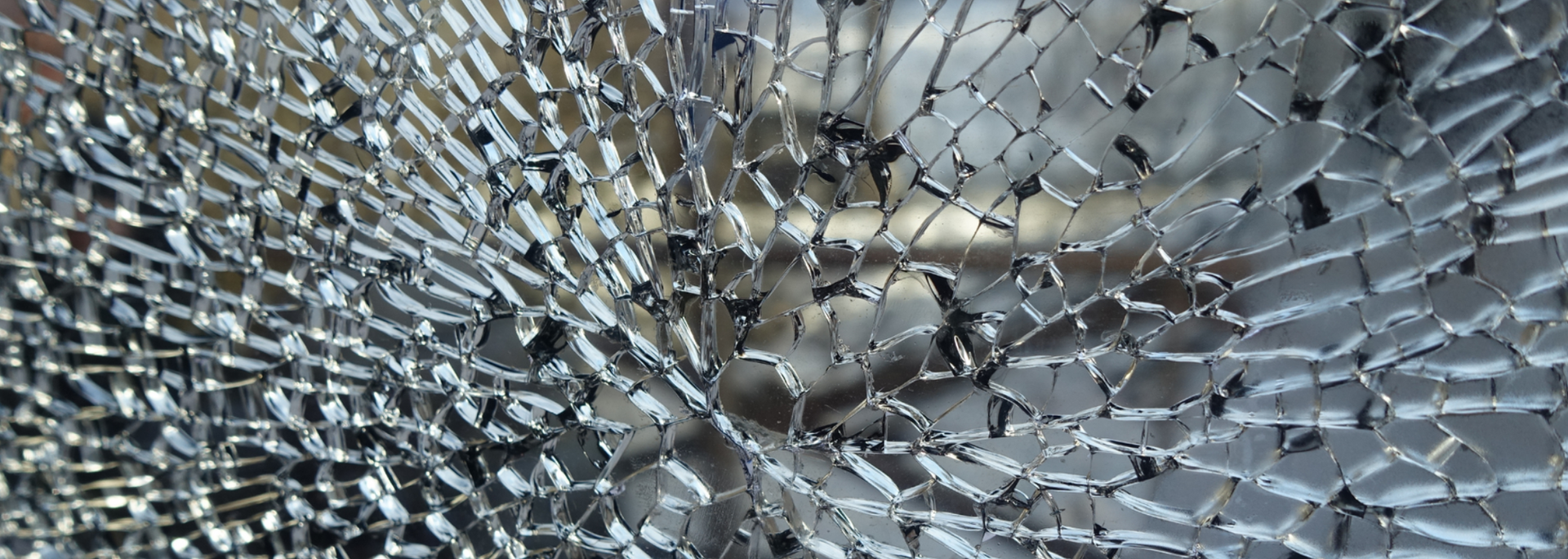 Close-up of shattered glass, showing intricate web of cracks and fragments reflecting light.